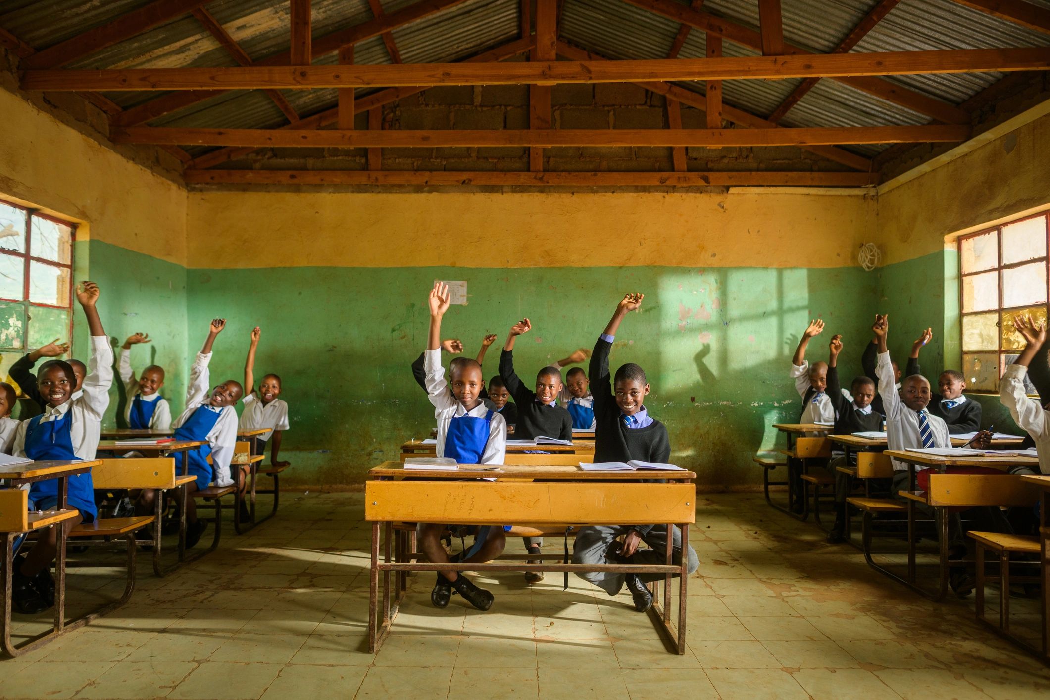Students in a classroom smiling and raising their hands